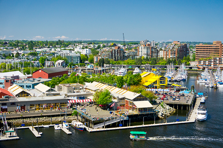 Family photo by the Granville Island waterfront with bridges and boats in the background.