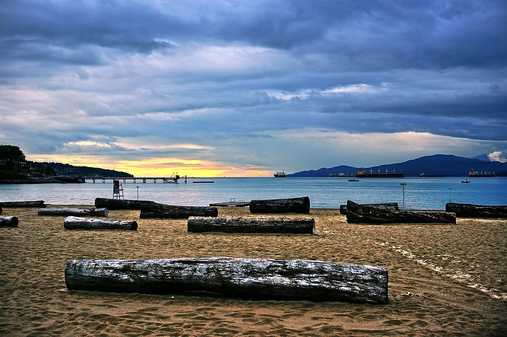 Family walking at Kitsilano Beach with Vancouver skyline at sunset.