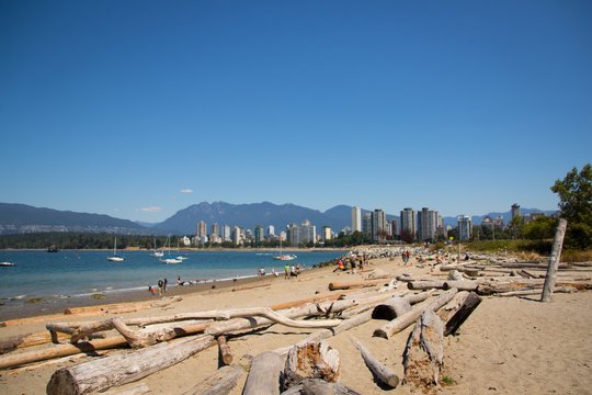 Couple at Stanley Park seawall with Siwash Rock and ocean background.