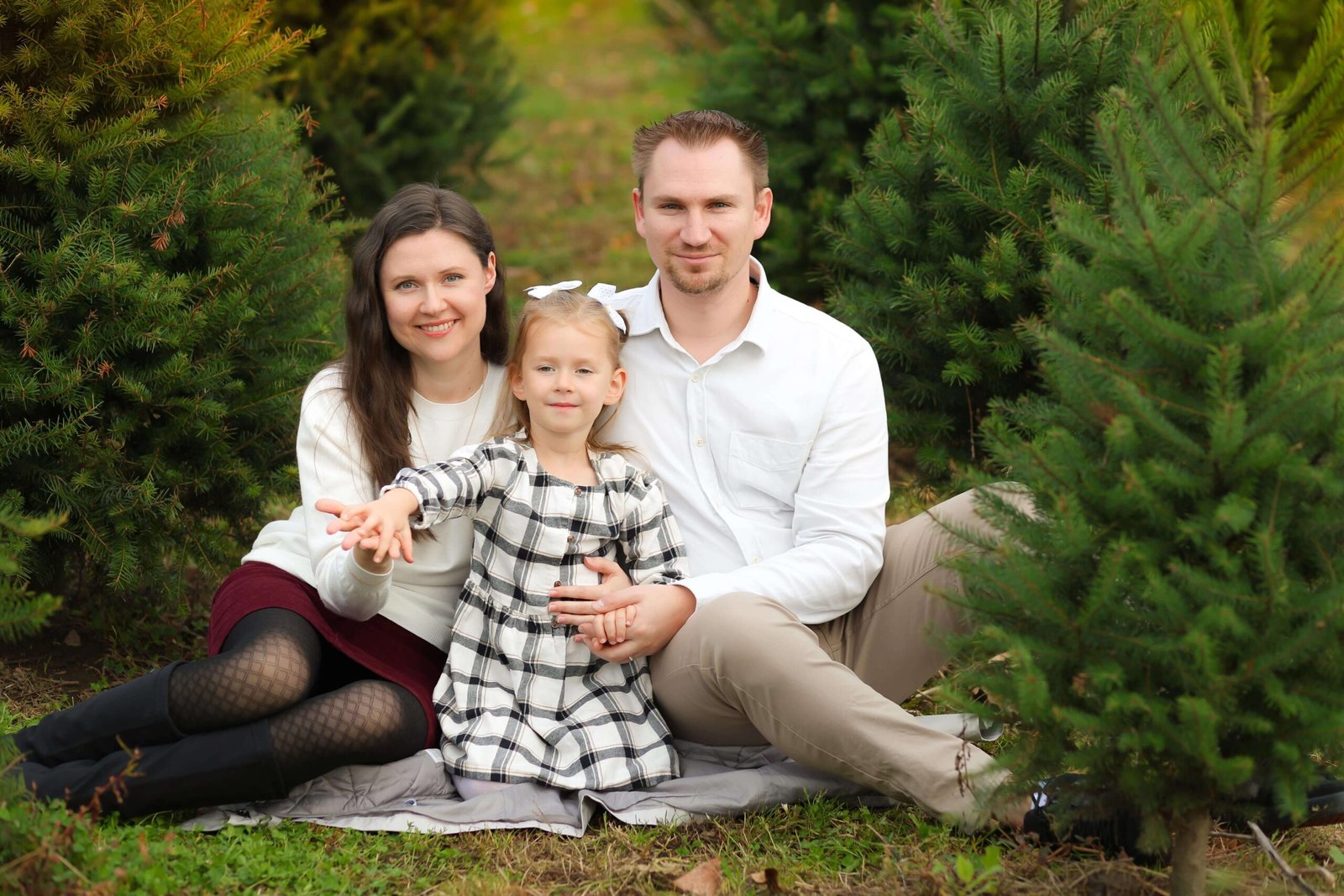 Parents and child sitting among Christmas trees