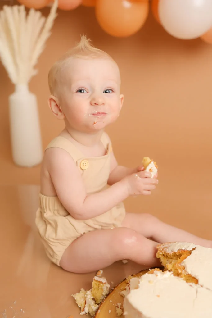 Baby sitting beside cake during first birthday session