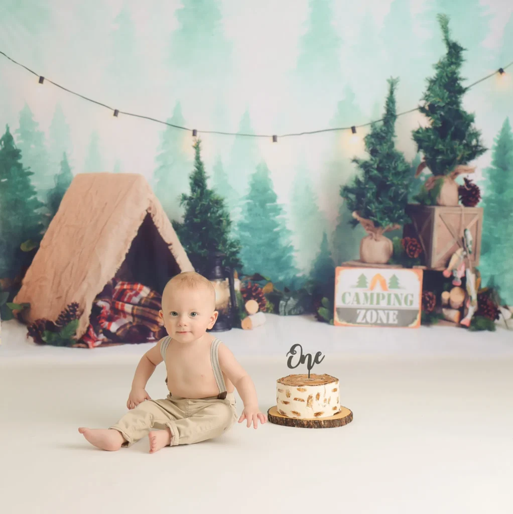 Baby sitting beside cake in woodland themed birthday setup