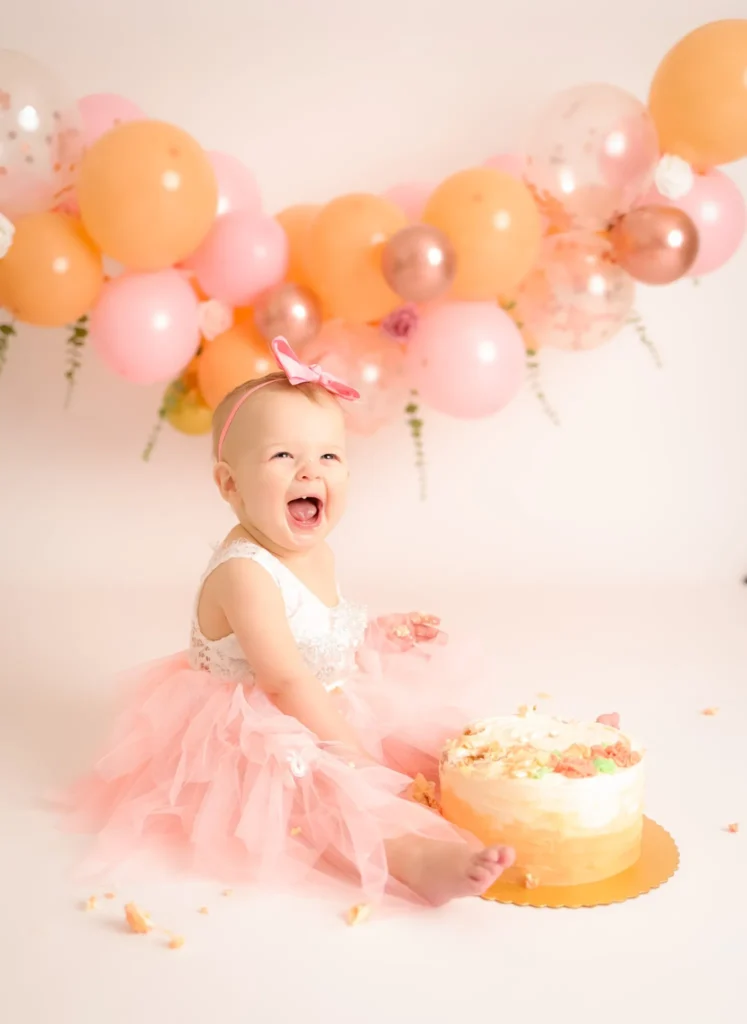 Baby sitting beside cake with peach balloon backdrop