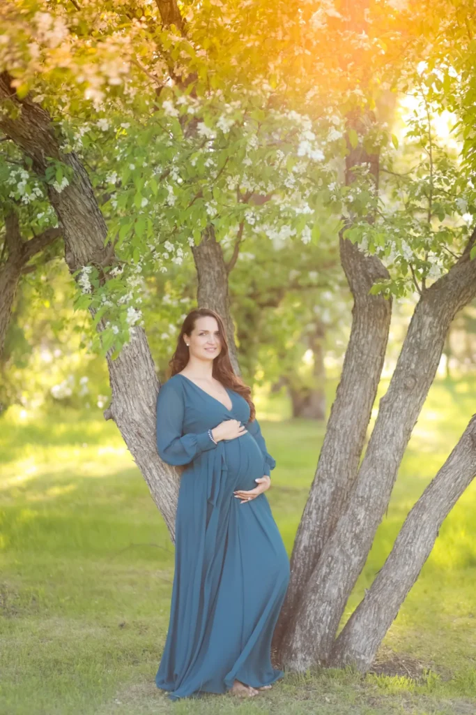 Pregnant woman standing under trees in flowing dress
