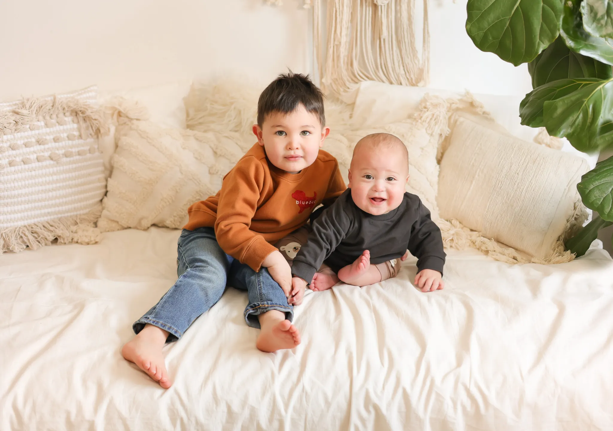 Two young children sitting together on bed smiling