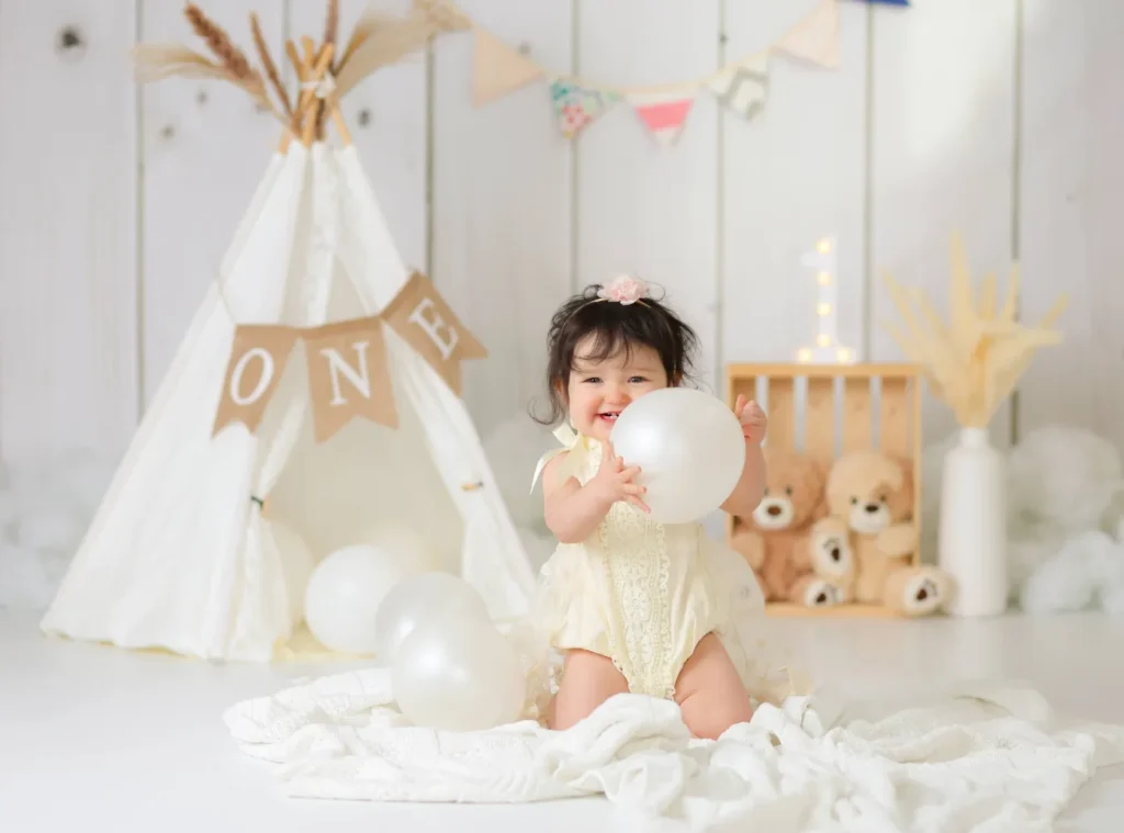 baby girl sitting with balloon teepee backdrop