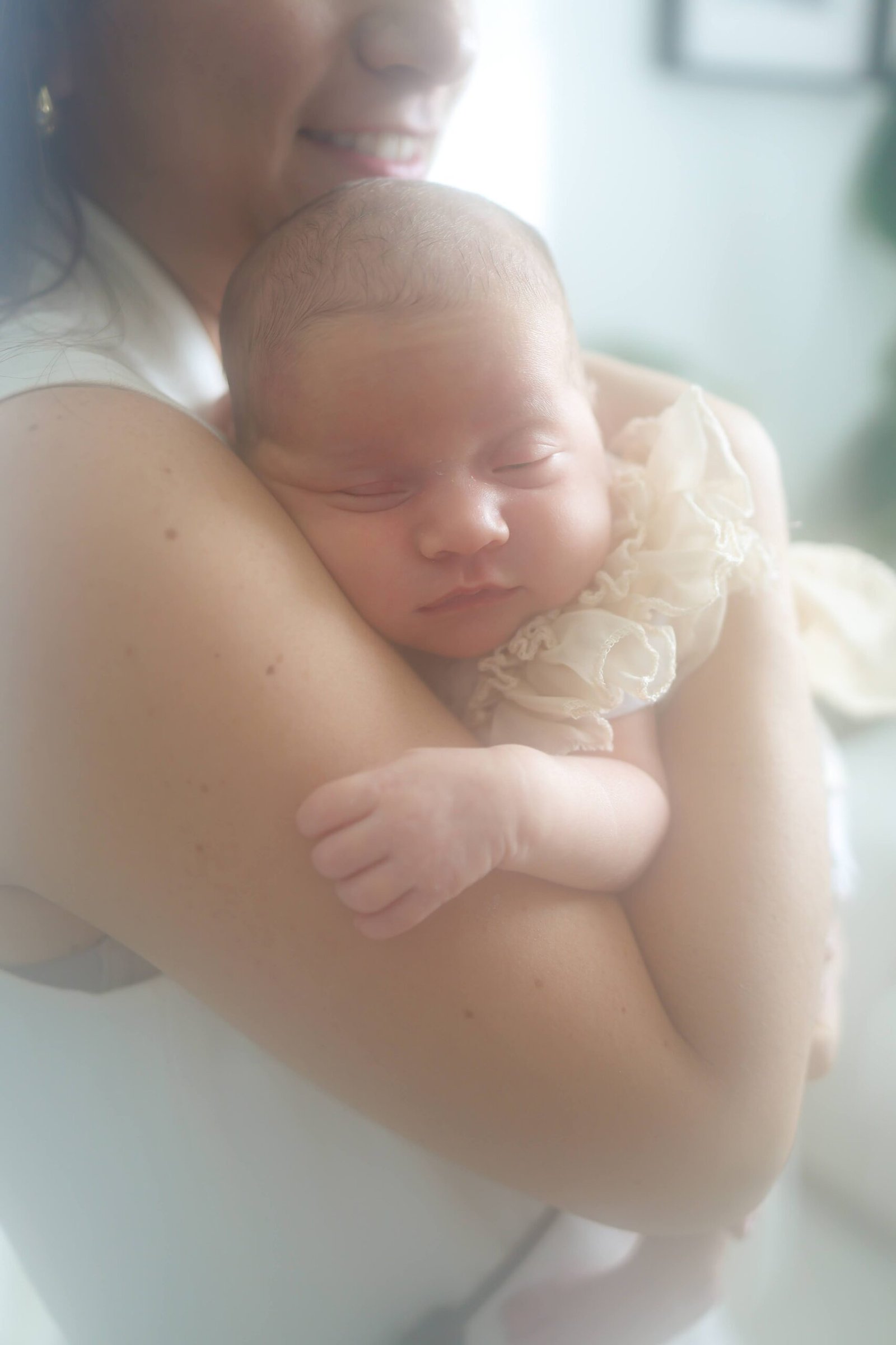 Mother holding her sleeping newborn in soft window light