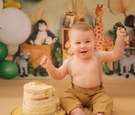 Baby clapping hands beside cake during birthday portrait
