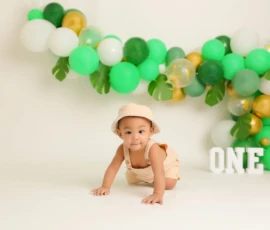 Baby crawling in front of balloon setup with number one sign