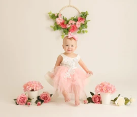 Baby sitting beneath floral arch with soft pink decor