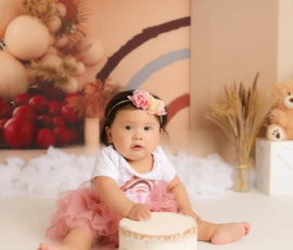 Baby sitting beside cake during first birthday photo session