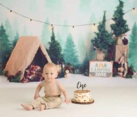 Baby sitting beside cake in woodland themed birthday setup