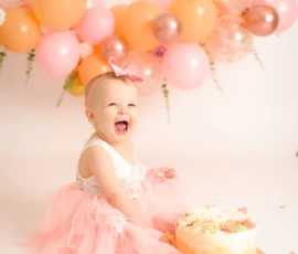 Baby sitting beside cake with peach balloon backdrop