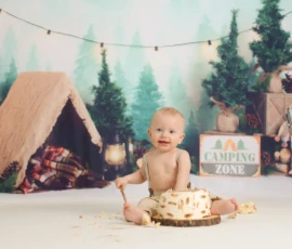 Baby sitting in woodland themed birthday setup with cake