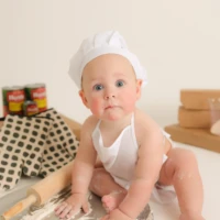 Baby sitting on floor wearing chef hat during milestone session Baby sitting on floor wearing chef hat during milestone session