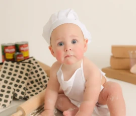Baby sitting on floor wearing chef hat during milestone session