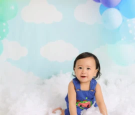 Baby sitting on floor with balloon backdrop during milestone session
