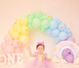 Baby sitting under pastel balloon arch during birthday sessio