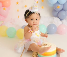 Baby sitting with cake and pastel balloon backdrop