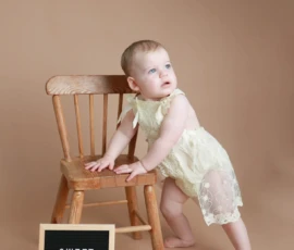 Baby standing beside chair with sweet one sign