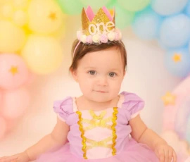 Baby wearing crown sitting in colorful balloon setup