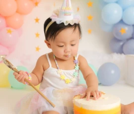Baby wearing crown sitting with colorful balloons and cake