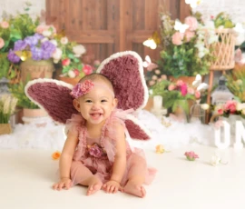 Baby wearing fairy wings sitting beside cake