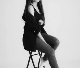 Black and white studio portrait of woman sitting on stool