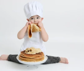 Child wearing chef hat sitting with stacked pancakes e1768938467218