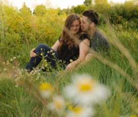 Couple sitting close together in tall grass during golden hour Couple sitting close together in tall grass during golden hour