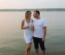 Couple standing together by water holding drinks Couple standing together by water holding drinks