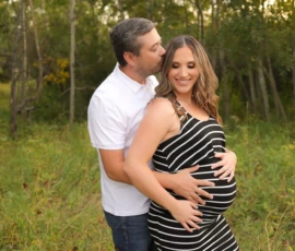 Expecting couple standing together outdoors holding belly stripe dress Expecting couple standing together outdoors holding belly stripe dress