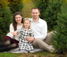Parents and child sitting among Christmas trees scaled 1 Parents and child sitting among Christmas trees scaled 1