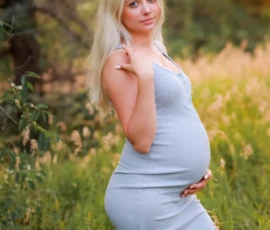 Pregnant woman standing in field wearing fitted dress Pregnant woman standing in field wearing fitted dress