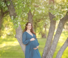 Pregnant woman standing under trees in flowing dress Pregnant woman standing under trees in flowing dress