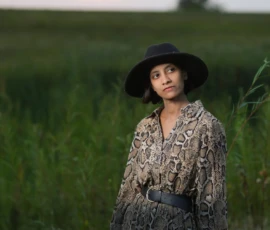 Woman standing alone in tall grass wearing wide brim hat